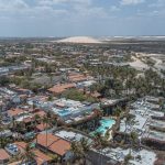 Vista aérea de Jericoacoara, com dunas, coqueiros e áreas de água próximas à vila.