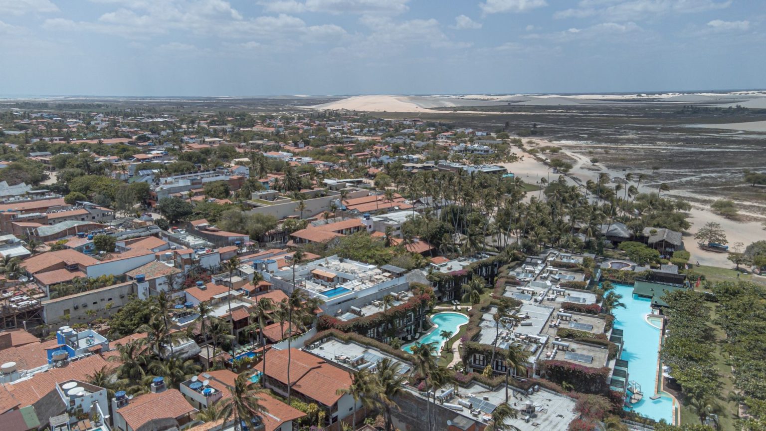 Vista aérea de Jericoacoara, com dunas, coqueiros e áreas de água próximas à vila.