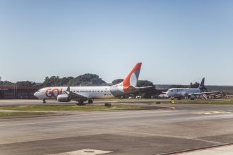 Aviões comerciais taxiando em um aeroporto sob céu ensolarado, antes da decolagem.