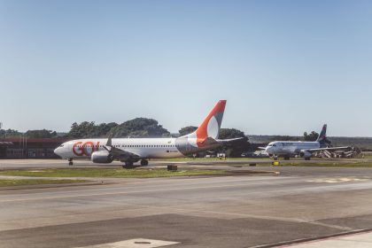 Aviões comerciais taxiando em um aeroporto sob céu ensolarado, antes da decolagem.