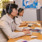 Agentes de atendimento ao cliente trabalham diante de computadores usando fones de ouvido em um escritório moderno.