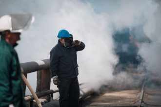 Trabalhadores industriais usando equipamentos de proteção em um ambiente com fumaça.