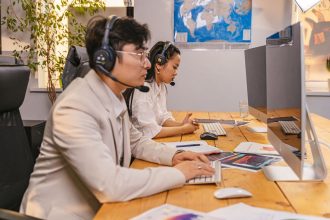 Agentes de atendimento ao cliente trabalham diante de computadores usando fones de ouvido em um escritório moderno.