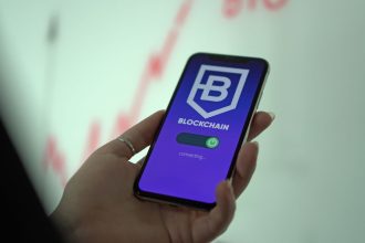 Mão segurando um smartphone exibindo uma carteira de criptomoedas em blockchain.