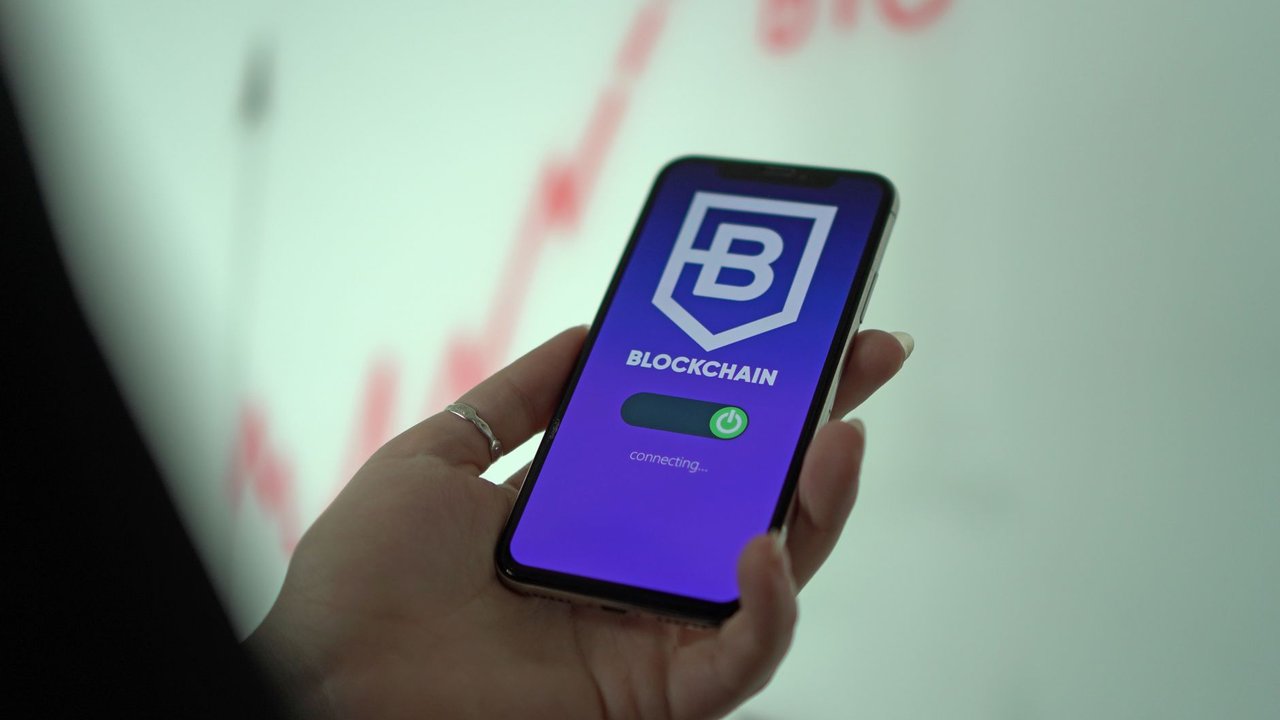 Mão segurando um smartphone exibindo uma carteira de criptomoedas em blockchain.